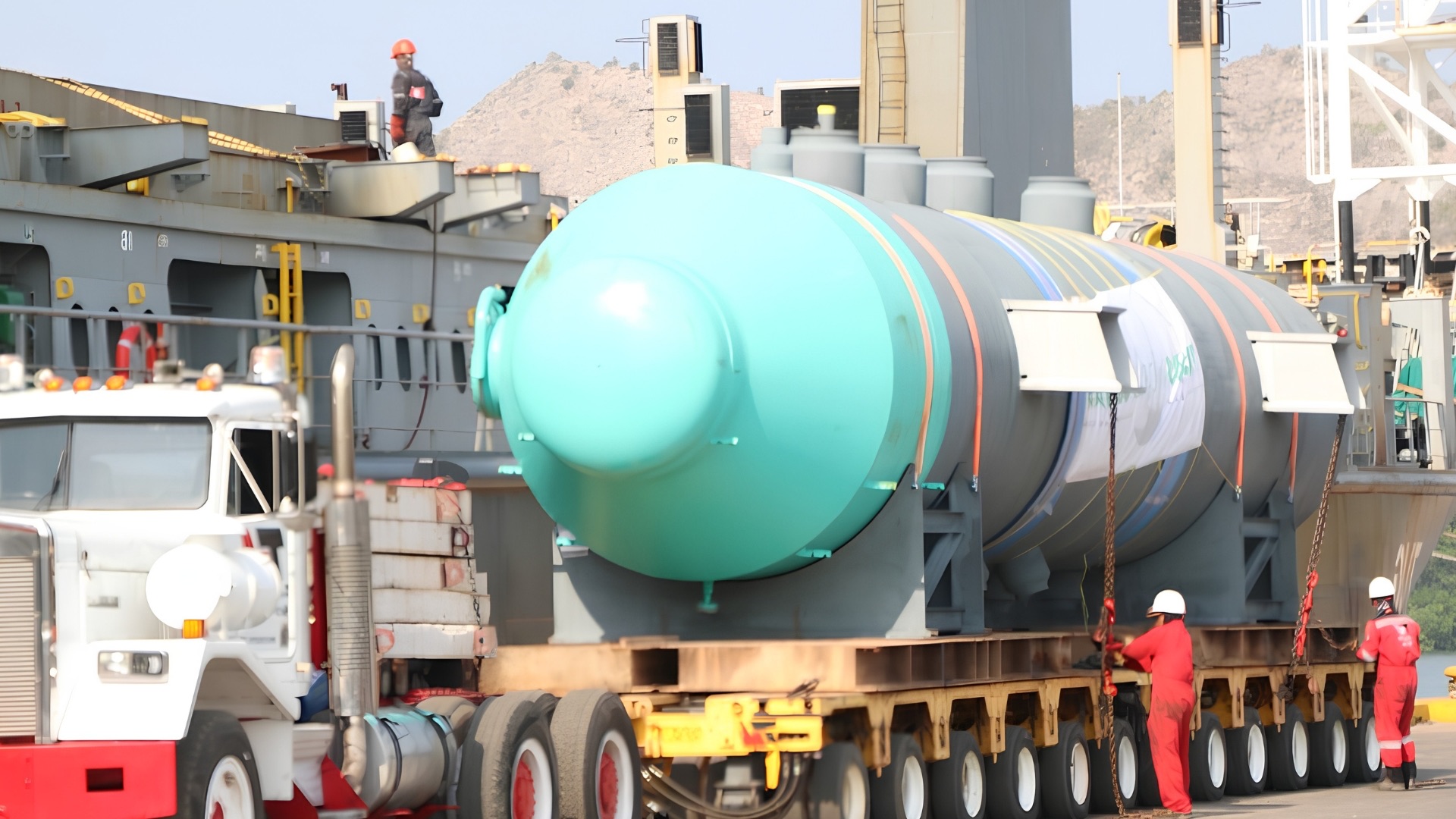 Carga de proyecto: tanque industrial de gran tamaño transportado en camión de plataforma junto al buque